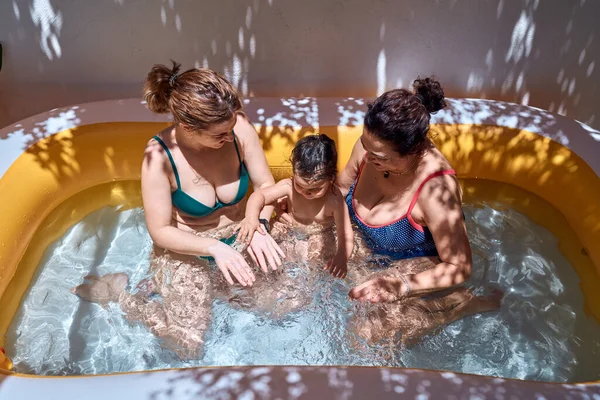 A girl, a grandmother and a little girl are playing in an inflatable pool. Vacation concept