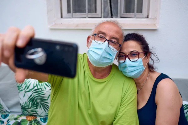 Cerrahi maskeli yaşlı bir çift cep telefonlarıyla selfie çekiyor. Maskeli selfie konsepti