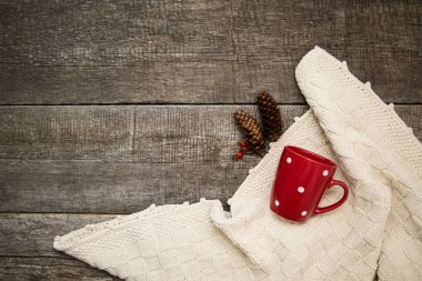 Bej örgü battaniye, kırmızı kupa, iki köknar konisi ya da üç yabani gül böğürtlenli eski ahşap arka planda kompozisyon.