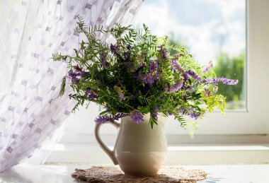 Pencerenin yanındaki beyaz sürahide bir buket kır çiçeği..