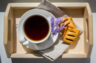 Kahvaltı manzarası. Tahta tepsi, beyaz fincan ve çay ve kurabiyeli çay tabağı..