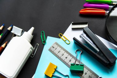 Çeşitli kırtasiye ürünleri siyah arka planda yatar. Okul, ofis kavramı.