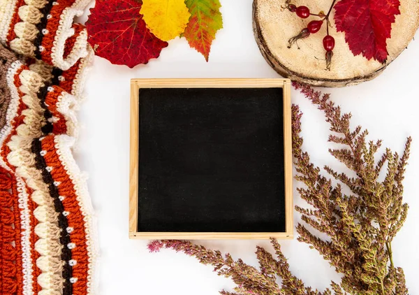 Autumn composition. Flat lay frame with slate background for notes, crocheted plaid, colorful leaves on a white background.