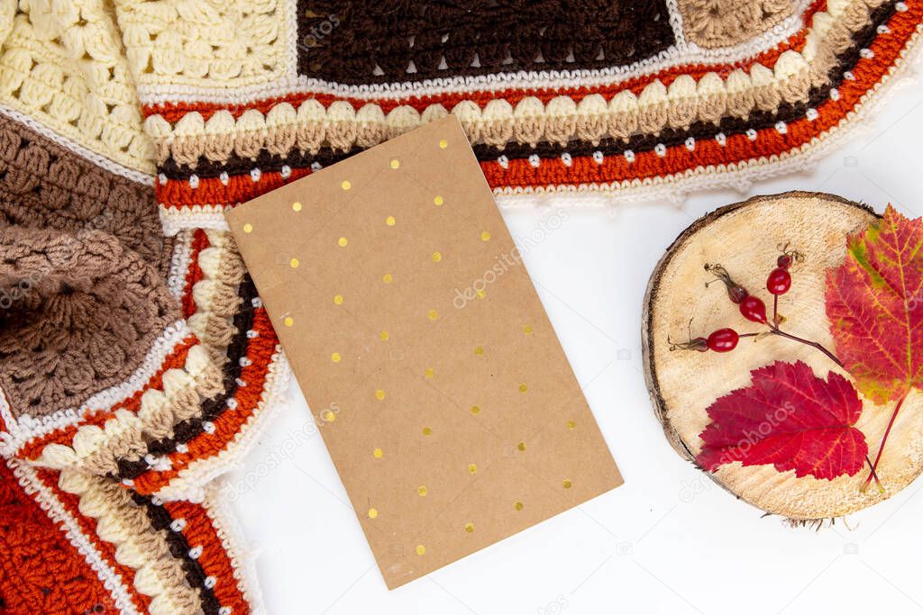 Autumn composition. Flat lay crochet plaid, colorful leaves, notepad.