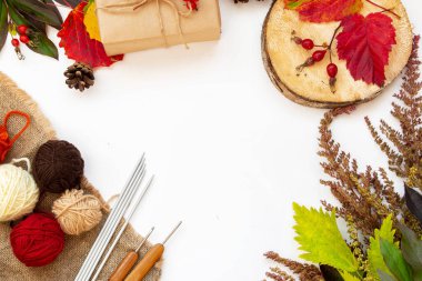 Sonbahar kompozisyonu. Sonbahar örgü konsepti. Uzayı kopyala Düz iplik topları örgü, örgü kancası, örgü iğneleri, el işi kağıdında hediye, sonbahar yaprakları ve çimenler, beyaz bir arka planda..
