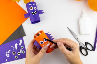 Cadılar Bayramı süsü. DIY ve çocukların yaratıcılık konsepti. Adım adım: Turuncu ve mor kağıtlardan oluşan tuvalet kağıdından canavar yap. 15. adım Kaşları çiz.