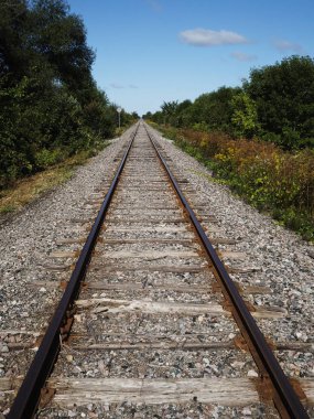 Parlak mavi gökyüzü ve beyaz bulutlar ile kırsal bir sahnede Demiryolu rayları
