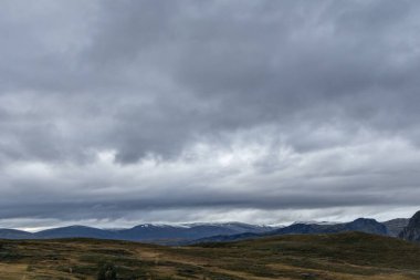 Dağ destansı bulutları, sonbaharda Norveç 'in manzara gezisi Tindevegen' e bakıyor. Dramatik gökyüzü bulutları ve mavi tepeler