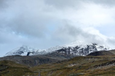 Dağlar beyaz kar tepeleri ve kayalarla, yüksek zirveler Norveç 'te seyahat, Tindevegen' de destansı bulutlar