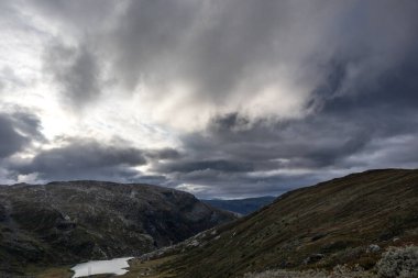 Dağ destansı bulutları, sonbaharda Norveç 'in manzara gezisi Tindevegen' e bakıyor. Dramatik gökyüzü bulutları ve mavi tepeler