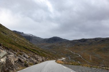 Karlı tepeli dağ yolu. Arabayla Norveç 'i dolaşmak, Tindevegen' de bulutlu sonbahar manzarası
