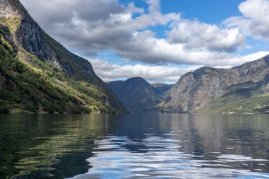 Su yüzeyinden parlak bir yansımayla bak. Norveç Aurlandsfjord seyahati, kano turu. Doğa, dağlar, mavi manzara, bulutlu destansı manzara.