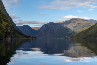 Su yüzeyinden parlak bir yansımayla bak. Norveç Aurlandsfjord seyahati, kano turu. Doğa, dağlar, mavi manzara, bulutlu destansı manzara.