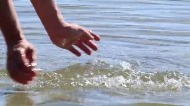 Yavaş çekimde, parlak güneş ışınlarına mavi su sıçrayan ellerin yakın çekimi. Suda neşeli bir ruh hali
