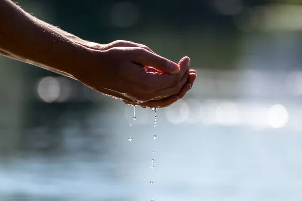Close-up of hands cupping sea river water with blurred bokeh background. Grabbing pure water in hands drops dropping into the water surface
