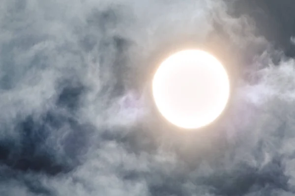 Big bright sun circle in cloudy sky in day time. Sun in white fluffy clouds close-up background in grey blue colors