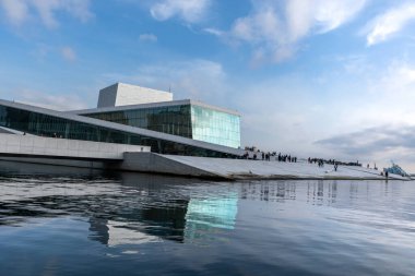 Norveç 'teki Oslo Opera Binası. Binanın modern mimarisi beyaz granit ve güzel cam ve su yansımalarıyla parlak mavi güneşli gökyüzüne manzaralı bulutlar yansıyor..
