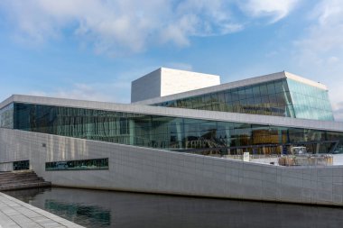 Norveç 'teki Oslo Opera Binası' nda insan yok. Binanın modern mimarisi beyaz granit ve su yansımaları ile parlak mavi gökyüzü manzaralı bulutlar.