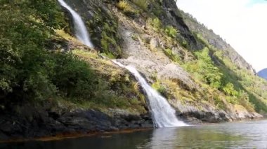 Şelale düşüyor, Norveçli fiyort Aurlandsjord su aynası yansıması. Norveç 'in vahşi dağlarının parlak manzarası. Güneşli yolculuk günü videosu.