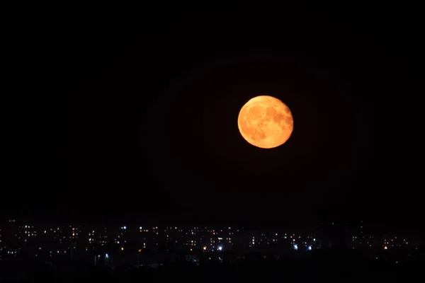 红色的大橘红色月亮在城市灯光上方的夜空中升起 漆黑的夜空和灿烂的大月亮 — 图库照片