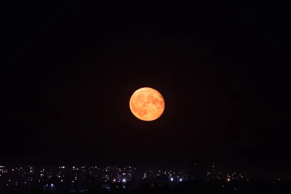 明亮的大橙色满月在城市灯光上方的夜空中升起 神秘的夜晚 漆黑的天空 大月亮 黑暗的宁静 — 图库照片