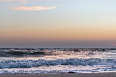 Fırtınalı beyaz dalgalarla gün batımı gökyüzü deniz kıyısında kumsal renginde.