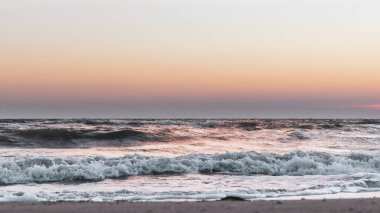 Fırtınalı beyaz dalgalarla gün batımı gökyüzü deniz kıyısında kumsal renginde.