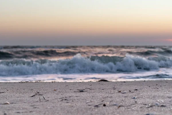 Deniz kıyısı kumsalına yakın çekim, günbatımı gökyüzü ve fırtınalı beyaz renkli parlak dalgalar.