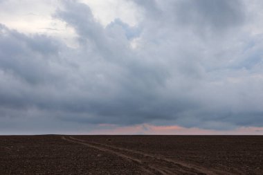 Sonbahar ekili kırsal arazi toprak yol ufka doğru ilerliyor dramatik gündoğumu renkli muhteşem bulutlar. Gri destansı günbatımı katmanlı bulutlu tarla