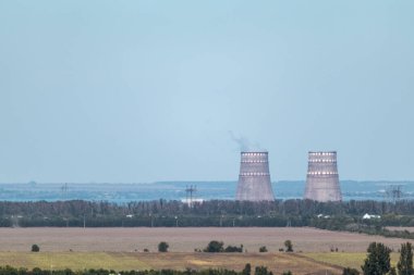 Uzakta iki büyük fabrika borusu olan mavi kırsal alan. Sanayi dumanı havayı kirletiyor.