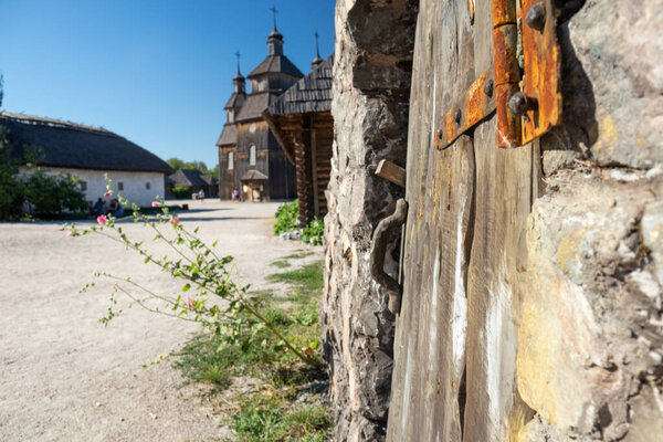 Wooden house door close-up and vintage church in Zaporozhian Sich medieval village, state of Cossacks on Khortytsia island, Ukraine. Sunny blue bright clear day