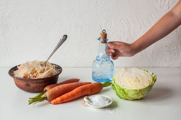 Persiapan sauerkraut, mangkuk tanah liat dengan sauerkraut di atas meja putih. Tangan Mans memegang botol . — Stok Foto