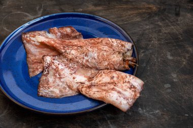 İki mürekkep balığı leşi, mavi bir tabakta, koyu bir arka planda.