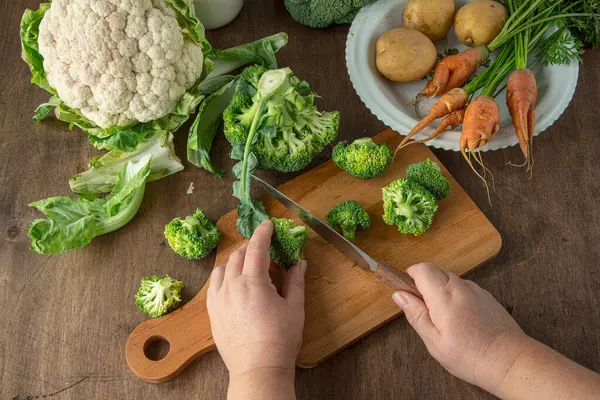 Membuat sup brokoli. pria memotong brokoli. Di atas meja adalah wortel, kembang kol dan kentang. — Stok Foto