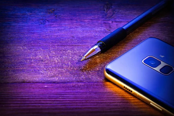 木製の背景にペンと青の携帯電話 — ストック写真