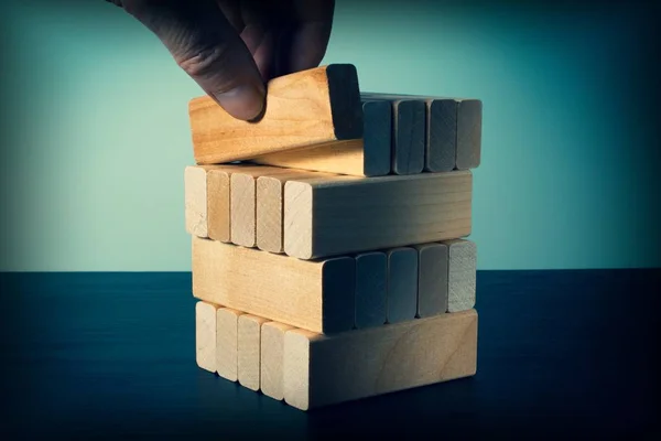 A hand places wooden blocks in a stack. Business concept for process growth success.