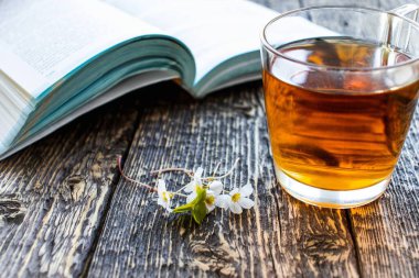 Yabani çiçekler, bir fincan çay ve ahşap bir yüzey üzerine açık bir kitap.