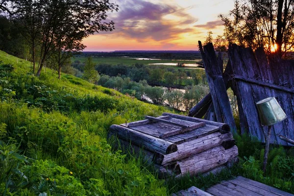 Beautiful landscape with a rustic well on a hill against a sunset.