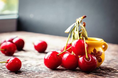 Eski ahşap bir yüzey üzerinde kiraz çilekleri ve sarı kil çömlek ile sakin bir hayat