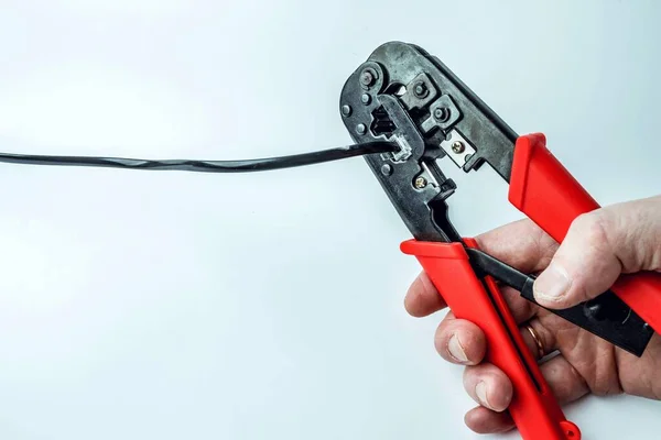 Hand of a craftsman with a crimping tool connecting an RJ45 connector with a black cable on a white background. Networks and telecommunications