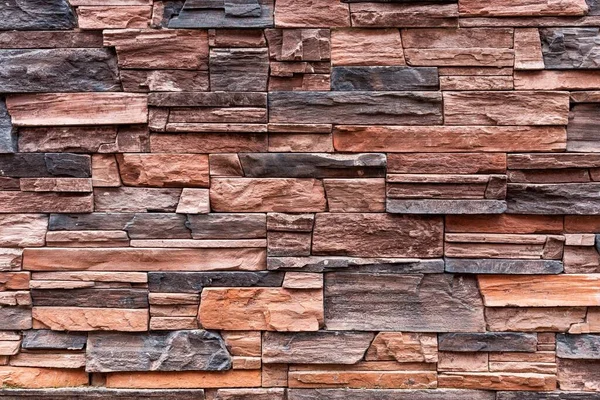 Background texture of decorative wall cladding made of stone of different colors, the effect of a natural rough flat stone. Fragment of decorative stone masonry.