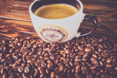 Tahta arka planda bir fincan kahve ve kahve çekirdeği.