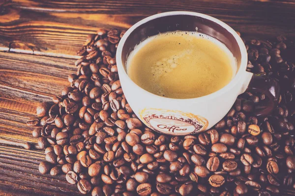 Tahta arka planda bir fincan kahve ve kahve çekirdeği.