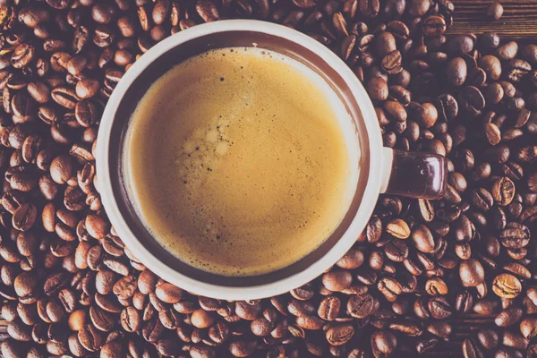 Tahta arka planda bir fincan kahve ve kahve çekirdeği.