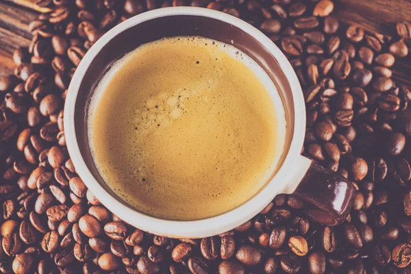 Tahta arka planda bir fincan kahve ve kahve çekirdeği.