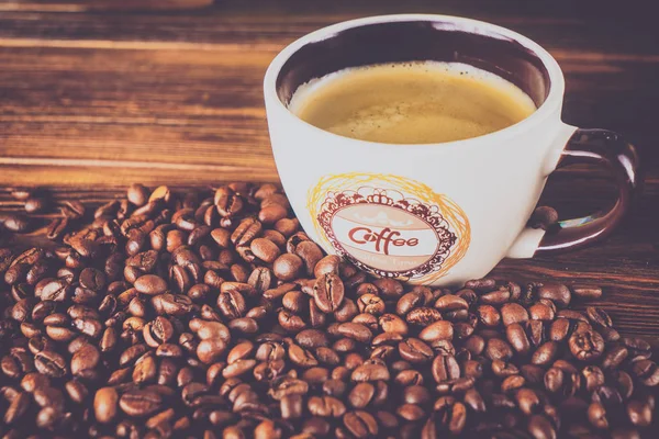 Tahta arka planda bir fincan kahve ve kahve çekirdeği.