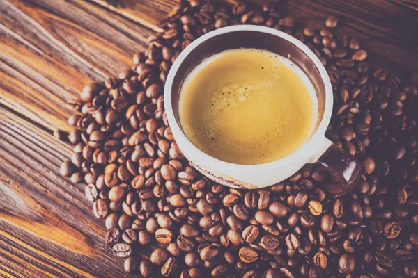 Tahta arka planda bir fincan kahve ve kahve çekirdeği.