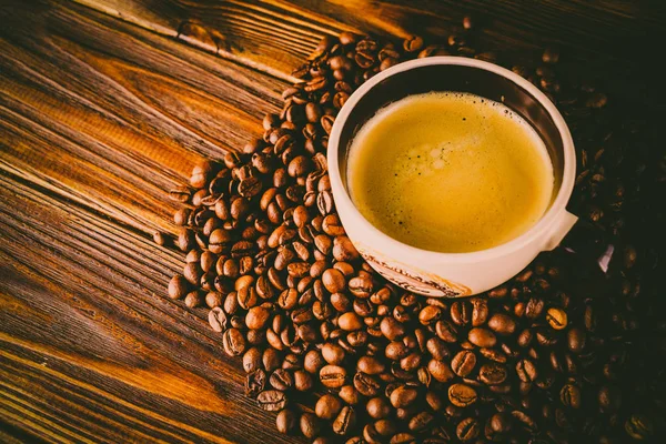 Tahta arka planda bir fincan kahve ve kahve çekirdeği.