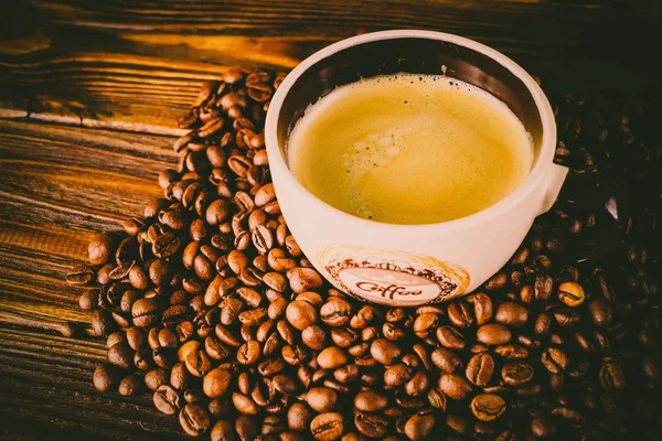 Tahta arka planda bir fincan kahve ve kahve çekirdeği.
