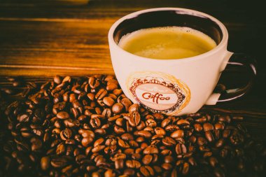 Tahta arka planda bir fincan kahve ve kahve çekirdeği.